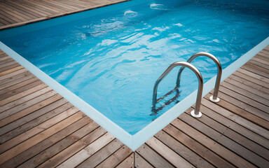 A refreshing swimming pool with a wooden deck and chrome ladder.
