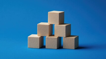 Obraz premium Wood blocks stacked as steps on a blue paper background, representing business growth, with plenty of room for adding text or graphics for marketing purposes.