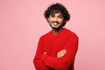 Side view young smiling happy Indian man he wearing red sweater casual clothes hold hands crossed folded look camera isolated on plain pastel light pink background studio portrait. Lifestyle concept.