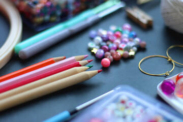 Colorful beads, coloring pencils, glitter, needles, string, hoop, tape and scissors on dark...