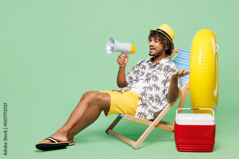 Wall mural full body young happy indian man he wear beach shirt hat rest near hotel pool sit in deckchair screa