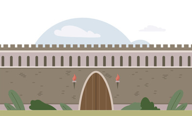 A stone castle wall stands tall with a large wooden gate flanked by two lit torches. Green vegetation appears in the foreground. Ideal for themes of medieval history historical architecture