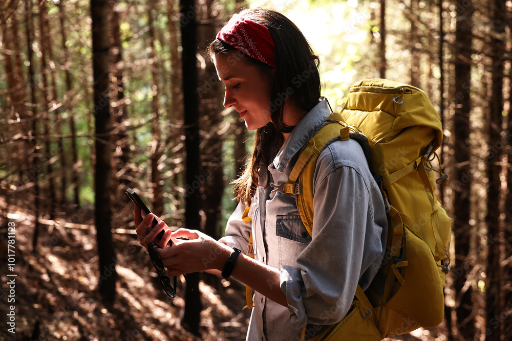 Poster Young hiker with backpack using smartphone in forest