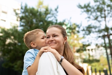 A joyful moment between a mother and son sharing affection in a bright park on a sunny day