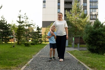 Mother and son enjoy a sunny day while walking together in a park filled with greenery and a clear blue sky