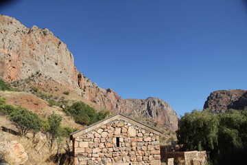 Small stone building in front of a rocky hillside under a clear blue sky.