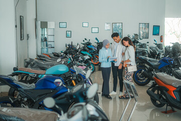 a couple chatting with a veiled saleswoman about the price list of a motorcycle in a showroom