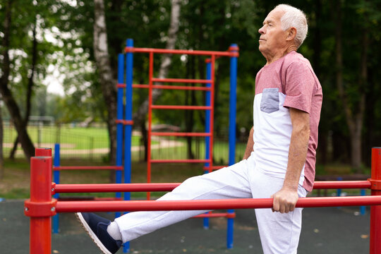 Elderly sportive man doing parallel bars exercise in park