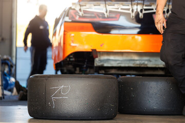 Racing slick tyres set against Nascar Whelen euro series racing sportscar vehicle Motorsport Arena garage box race track pit paddock hanged hydraulic  jack lift. European motor auto sport competition
