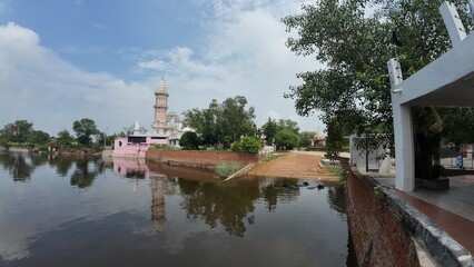 Tranquil pond in a village, showcasing a temple complex, embodying calmness and serving as a sacred pilgrimage destination. Haryana, India 