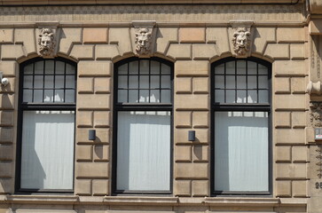 Facade of a historic building featuring three arched windows with ornate lion head sculptures and a classic stone design
