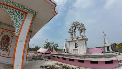  Exterior view of a Hindu temple with a towering structure against a backdrop of clouds and a clear sky