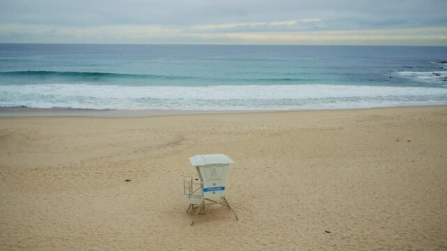 Wide shot on empty beach with small lifeguard station service or booth. No people in afternoon or early morning. Winter time in Sydney Australia beach shore. Cold quiet and windy day at the ocean