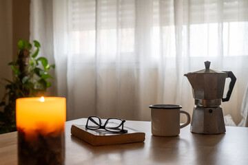 Create a Cozy Atmosphere with a Coffee Maker, a Warm Cup of Coffee or Tea by the Window, a Softly Glowing Candle, and an Engaging Book – Perfect for Relaxing Mornings.