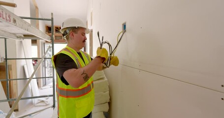 Dedicated construction worker, wearing a bright safety vest and a protective hard hat, is currently involved in crucial electrical work as part of a home remodeling project that is underway
