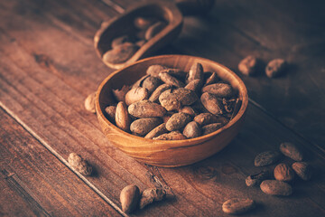 Organic cocoa beans in wooden bowl on wooden background