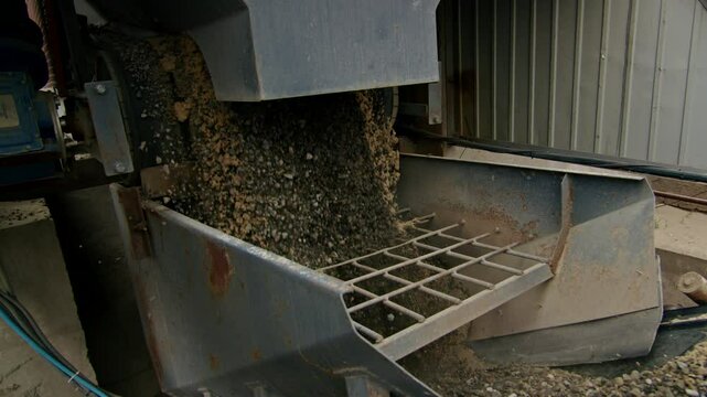 Gravel and sand being processed by industrial machinery in a manufacturing facility. Close-up of raw materials in production.