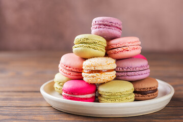 Multicolored macaroons in a plate on a wooden table.