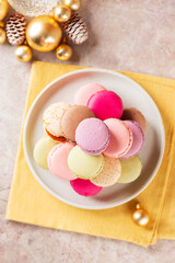 Macarons in a plate with Christmas balls on a yellow napkin. Christmas background. Vertical orientation, top view.