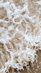 Obraz premium Ocean waves crashing on sandy beach, creating foam and texture in water.