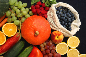 Round straw bag and various seasonal fruits and vegetables on dark background. Summer and fall produce. Top view.