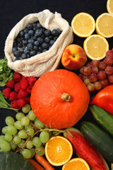 Round straw bag and various seasonal fruits and vegetables on dark background. Summer and fall produce. Top view.