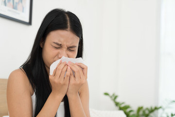 Young Asian woman feeling unwell and have a cough while sitting on the bed. Young woman have symptoms of illness and holding her mouth with her hand