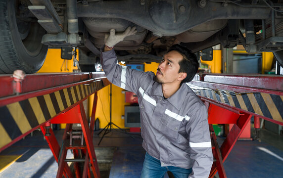 Young mechanic in gray uniform maintenance or inspection work on a vehicle that is raised on a lift.
