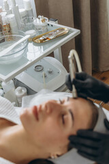 Professional dermatologist in medical gloves performs microdermabrasion on woman in a beauty salon