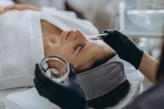 Cosmetologist performs a facial peeling procedure on a young woman.