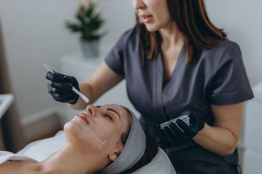 Cosmetologist performs a facial peeling procedure on a young woman.