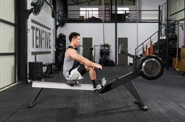 An athletic man in sportswear is engaged in an intense workout session on a rowing machine inside a well-equipped gym.