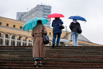People with colorful umbrellas climb the steps on a street. Rainy weather in autumn city