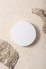 Natural cosmetic background for product presentation. Rocks and white podium on the sand. Top view.
