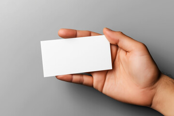 A hand holding a blank white business card against a plain gray background. The card is oriented horizontally and centered in the image.