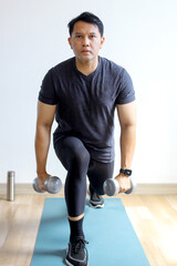 Portrait of Asian sporty man doing dumbbells workout at home, working on arms strength.