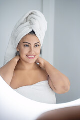 Beautiful woman is smiling while touching her neck and looking away after taking a relaxing shower