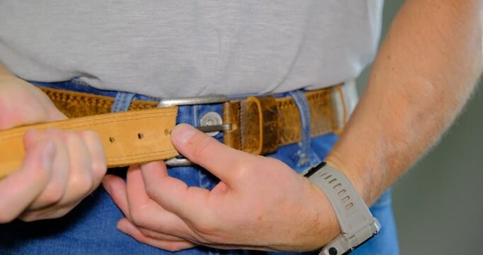 A man adjusts his belt to emphasize his fashionable style, to improve his appearance and fit.