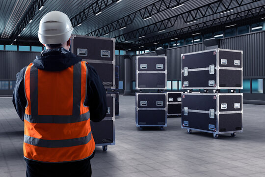 Containers on wheels inside hangar. Man looks at transport chests. ATA containers with filming equipment. Worker controls delivery of equipment standing back to camera. PLY boxes for filming crew