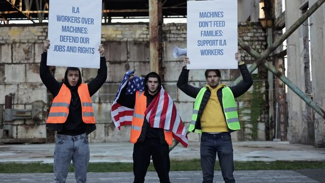 Three American protestors hold signs and the American flag during an anti-automation protest. People protesting against the introduction of robots and automation at their workplace.