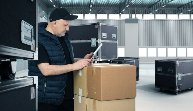 Boxes with musical equipment. Man sound engineer inside hangar. Guy with electronic tablet. Containers on wheels in exhibition center building. Man sound engineer preparing to install music equipment