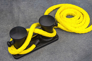 Obraz premium Mooring bollard. Yellow rope is tied around metal post. Mooring bollard on gray surface. Ship rope for securing boat at pier. Mooring bollard on yacht. Ship equipment close-up. Moored sea vessel