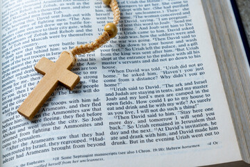 Wooden religion cross on rosary beads and opened blue book of Holy Bible. It is laying on a wooden table. Religious christian holiday. Symbol of faith in God, Christianity Feast