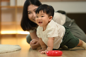 Cute little baby boy crawling on the floor with young mother watching her child with affection