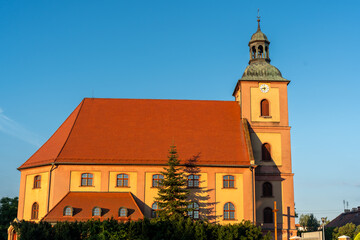 Fototapeta premium Historic church with a red roof and clock tower bathed in warm sunset light, set against a clear blue sky. High quality photo