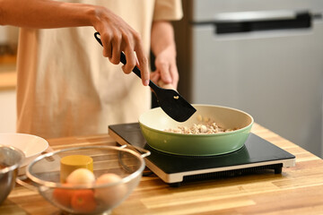Close up shot of young man cooking, stirring ingredients in frying pan with a spatula