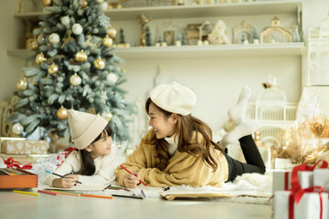 Happy mother and a little daughter drawing a picture Together Near Christmas Tree During Christmas Day