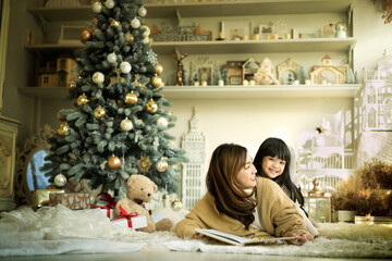 Smiling little girl embracing her mother on christmas day. Beautiful mother read story tale book to her daughter.