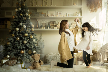 Happy mother and daughter dancing together on christmas. Cute girl having fun with her mom near christmas tree in Xmas day.