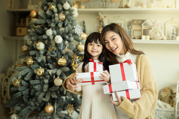 Merry Christmas, Mother and little daughter holding christmas presents with christmas tree in the background.